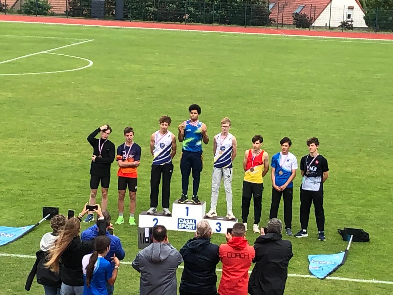 Remise de médailles à Caudry : huit jeunes athlètes autour d'un podium sur le terrain, des parents prennent des photos